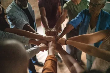 Group of people in a circle, placing their hands in the center of the circle.