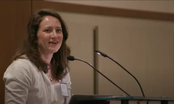 Woman in a cardigan smiling and speaking from a podium