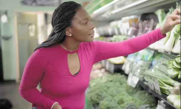 A young woman in the produce aisle of a grocery store, reaching out to the produce.
